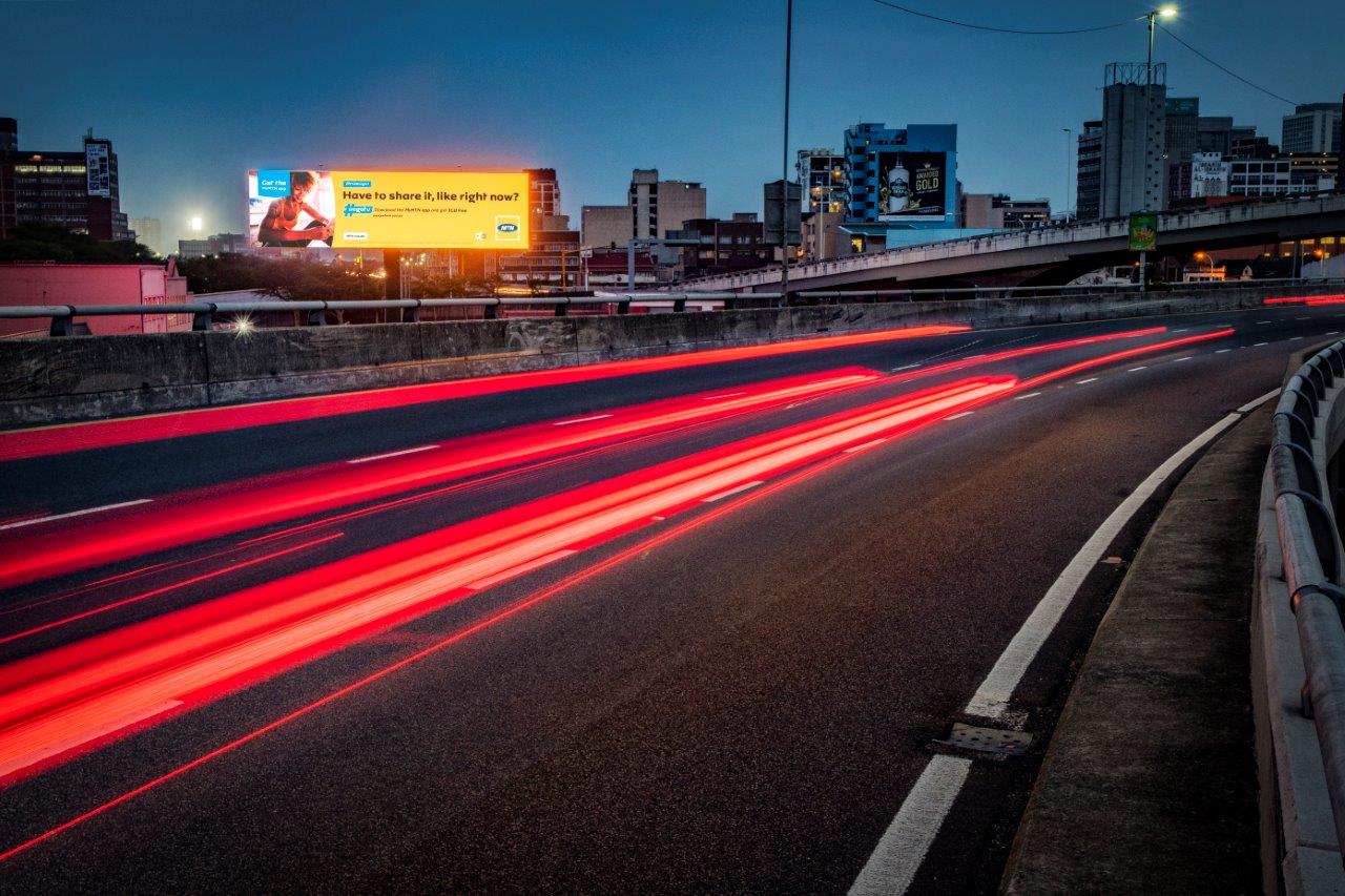 Illuminated highway billboards at dusk in South Africa with streaking car lights